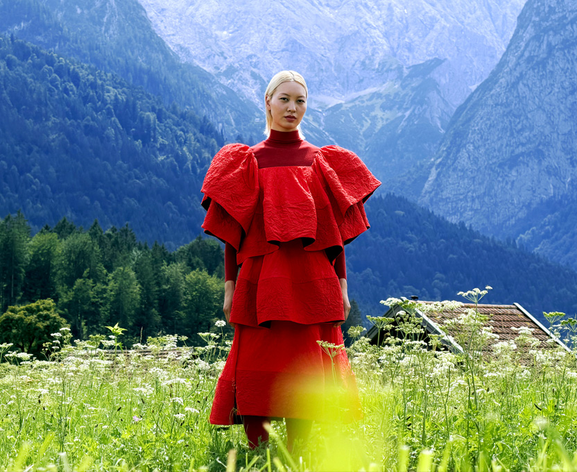 A model in a bright red dress stands in a mountain valley, showcasing the wide color gamut of Studio Display XDR